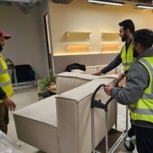 Removal team in high-visibility vests carefully moving sofas with a trolley during a professional relocation service.