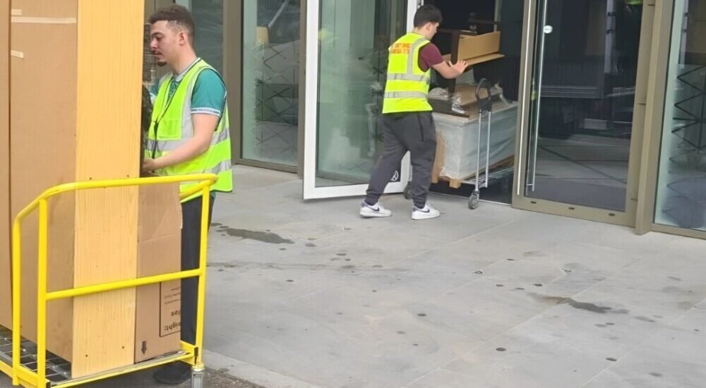 Professional movers transporting large furniture and boxes on trolleys during an office or house relocation service.