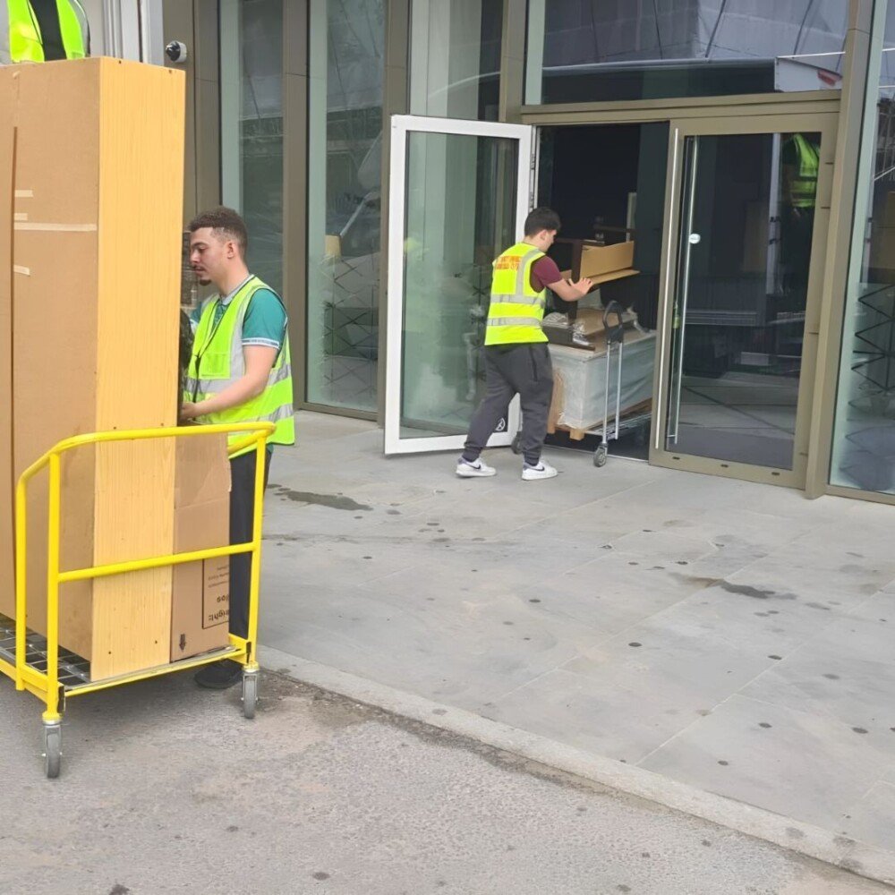 Professional movers transporting large furniture and boxes on trolleys during an office or house relocation service.
