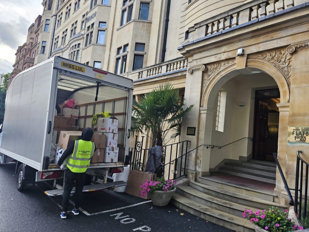 Removal company team unloading moving boxes from a van outside a residential building during a home relocation in London.